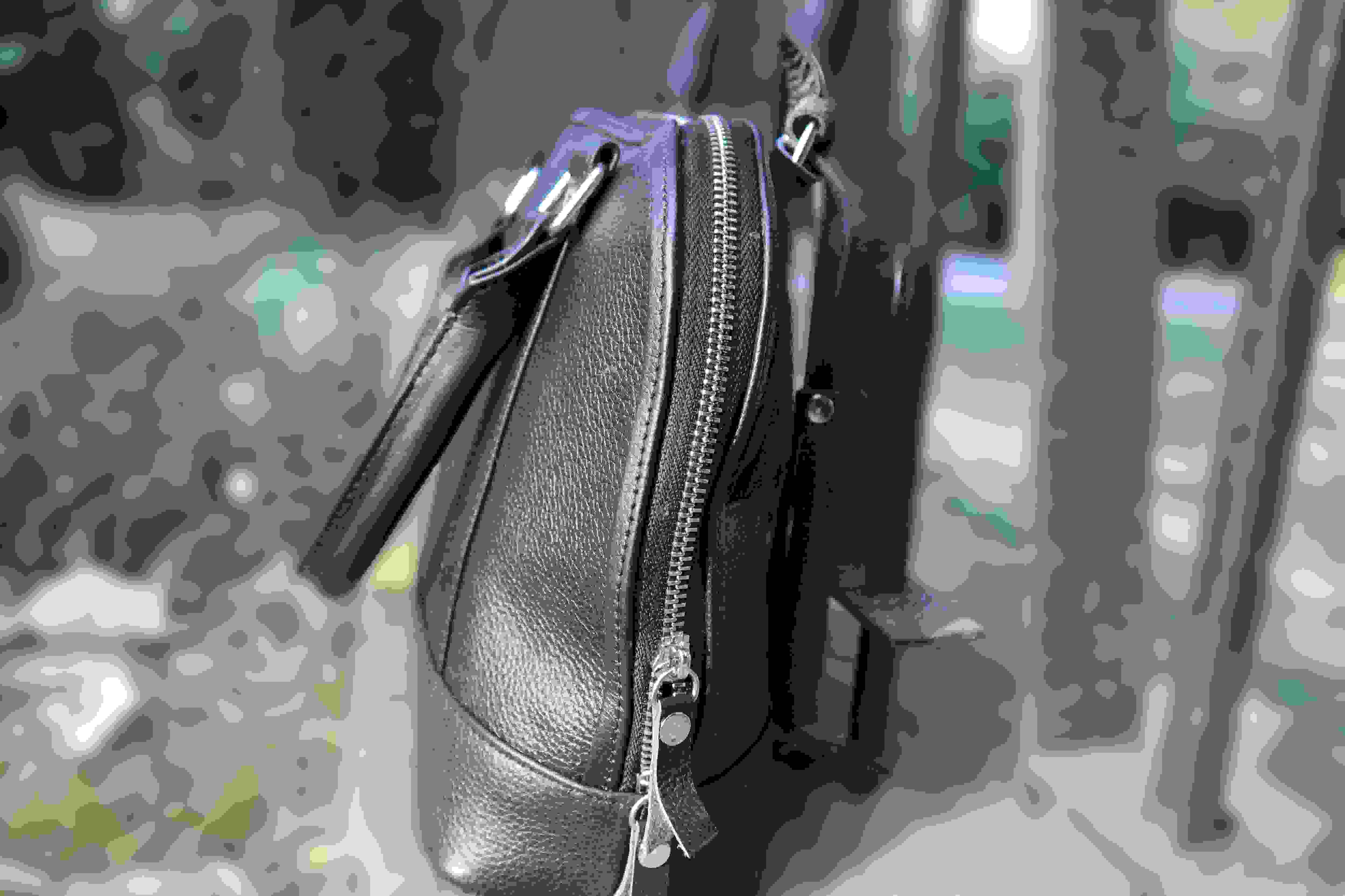 Black leather handbag with a zipper on a textured gray background
