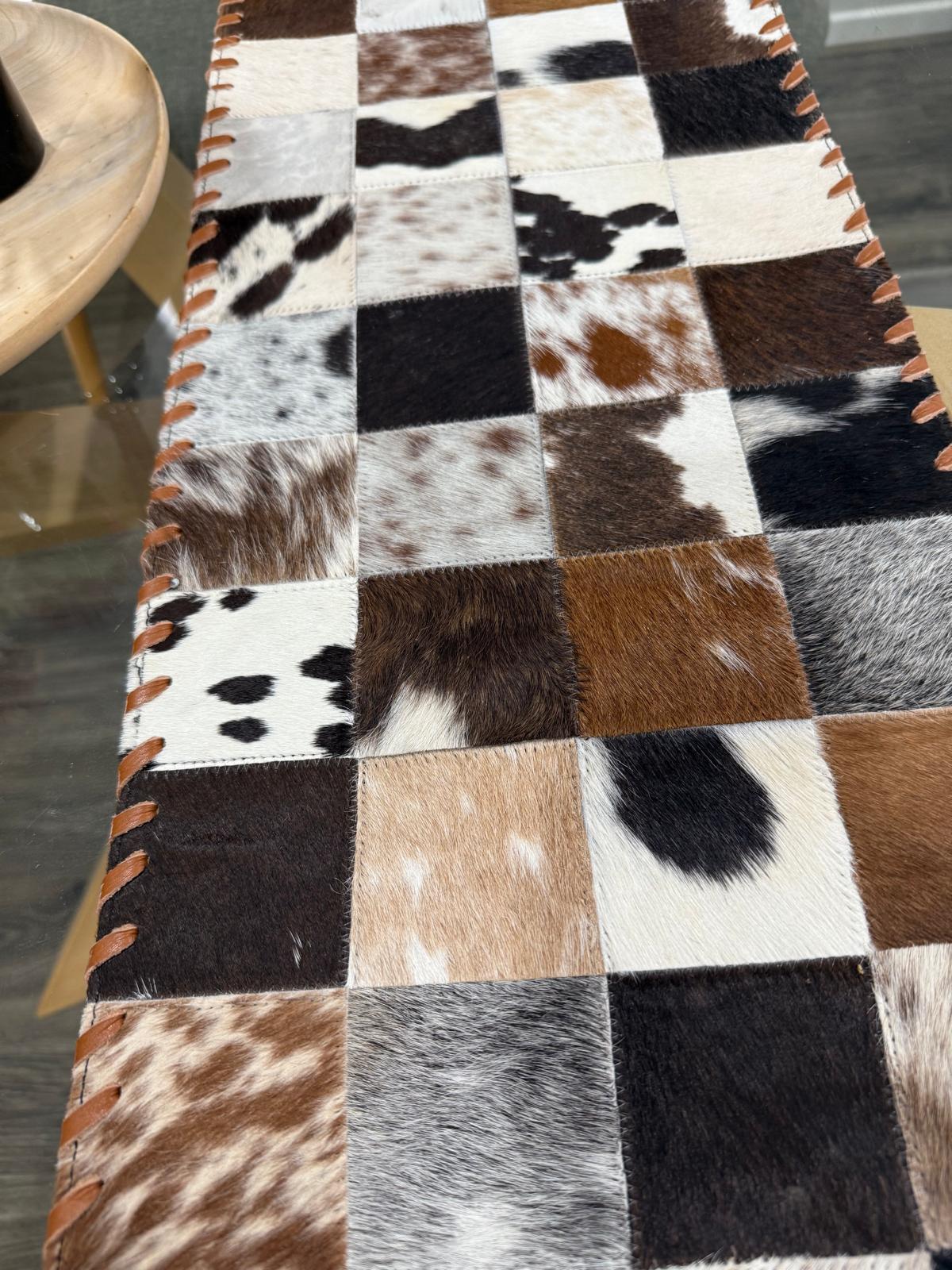 Patchwork cowhide rug with various brown, black, and white patterns on a wooden floor.