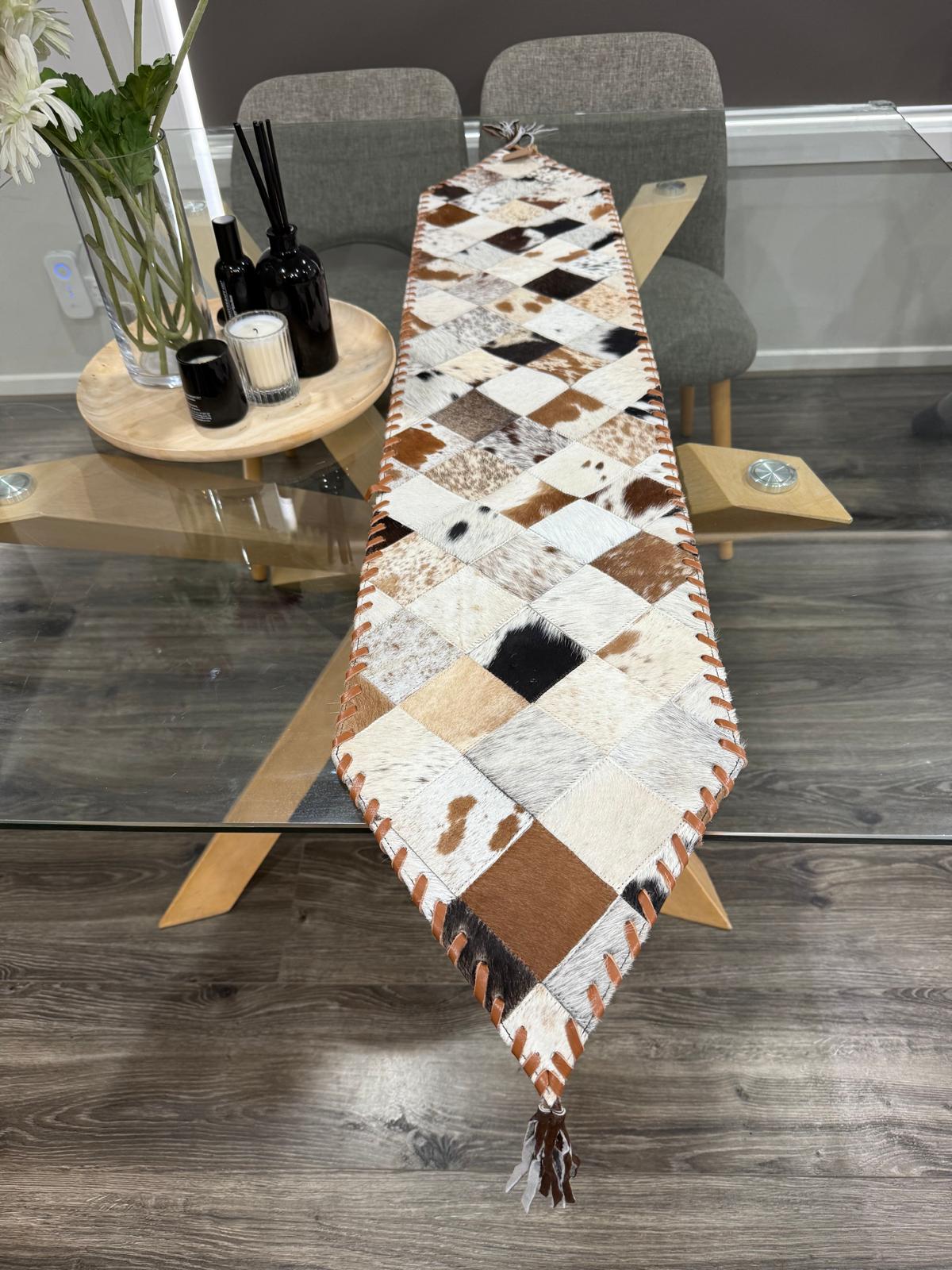 Patchwork cowhide table runner on a wooden dining table with chairs and decor items.