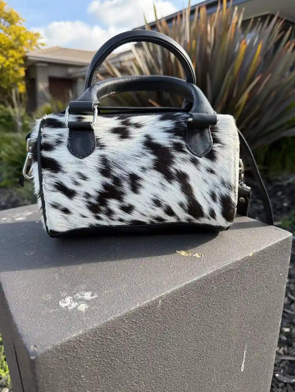 Black and white cowhide handbag on a stone ledge with outdoor background