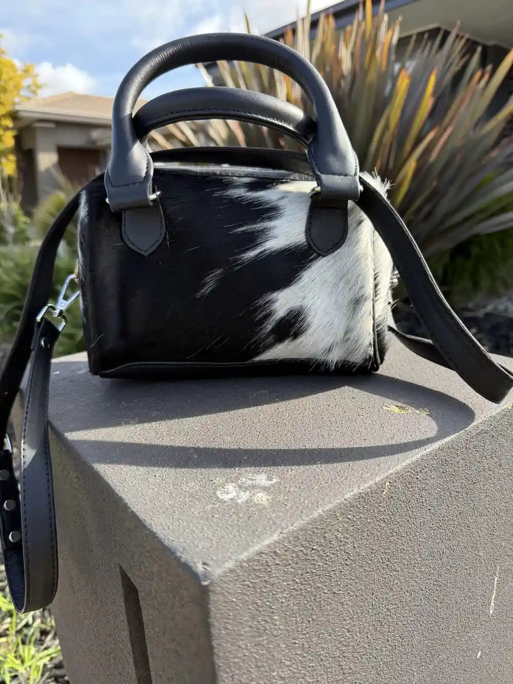 Black and white cowhide handbag on a stone surface with plants in the background