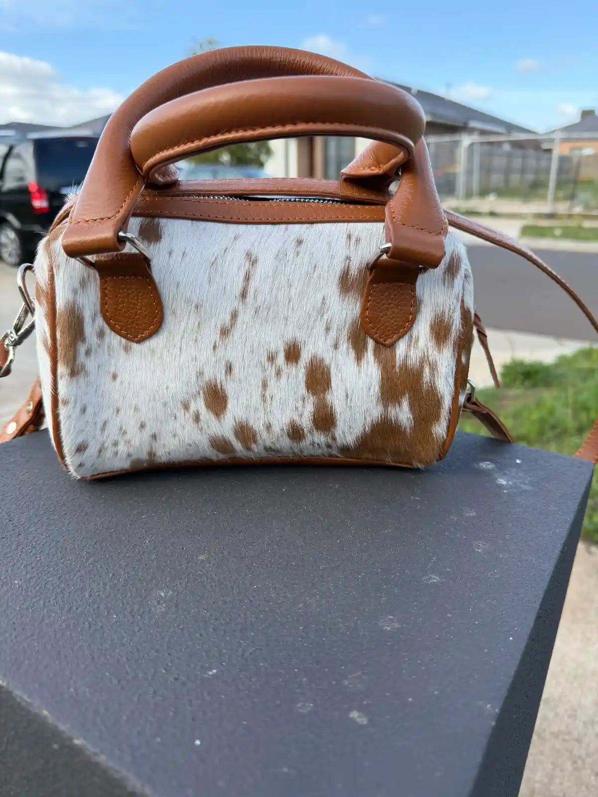 Cow print handbag with brown handles on a black surface outdoors