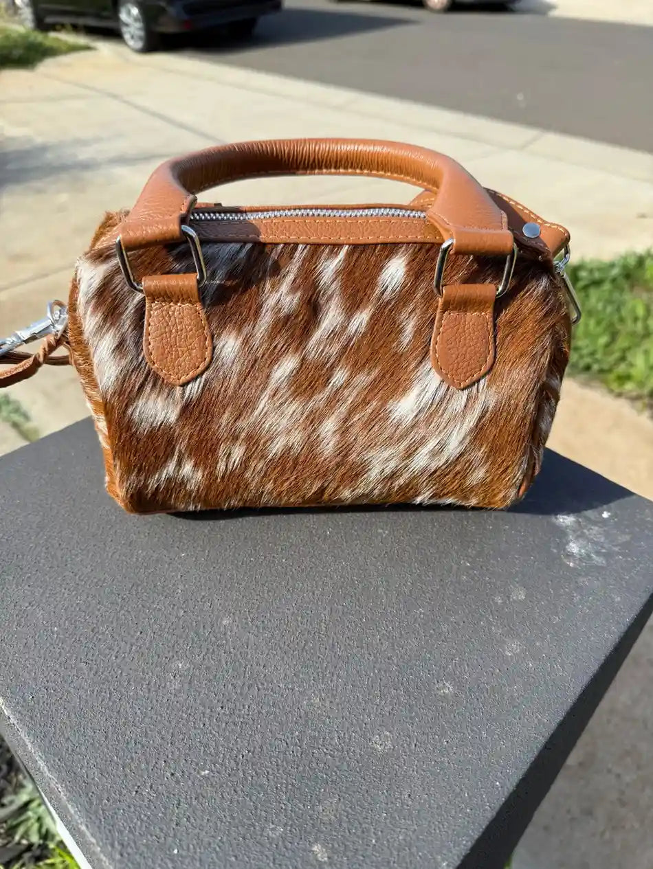 Brown and white cowhide handbag on a gray surface with a blurred background