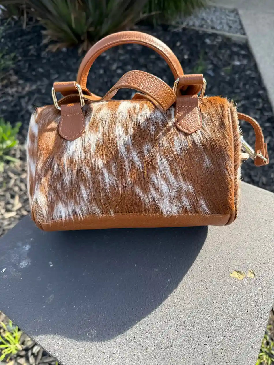 Brown and white cowhide handbag on a concrete surface with grass in the background