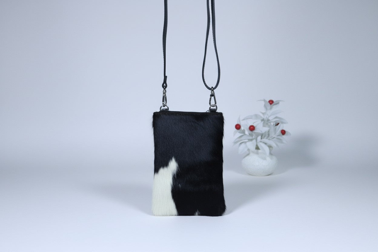 Black and white cowhide crossbody bag on a light gray background