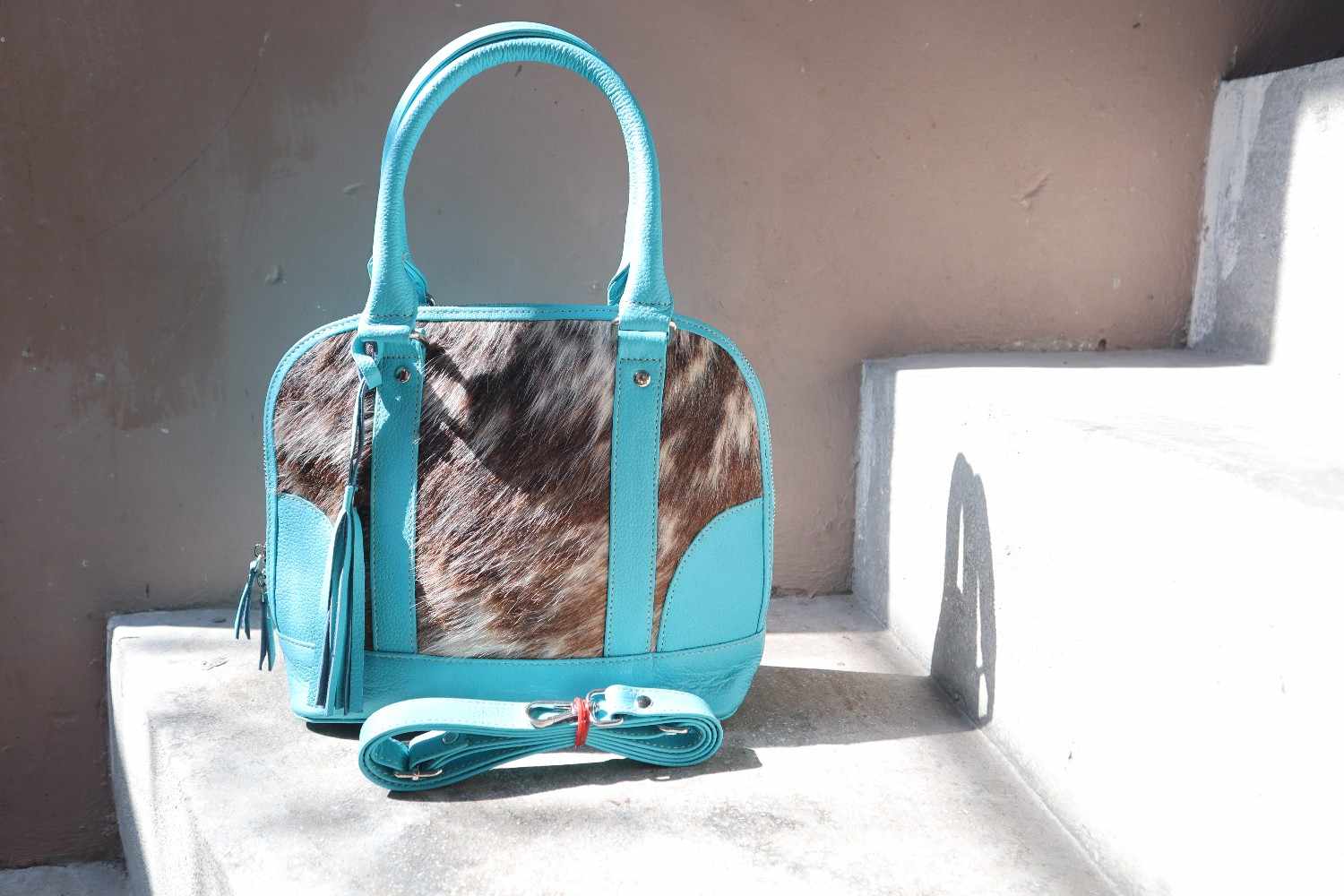 Turquoise handbag with cowhide pattern on a white surface