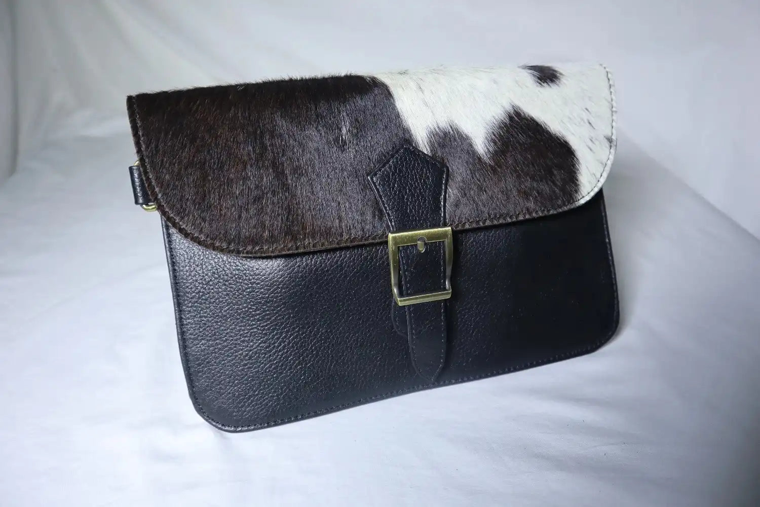 Black and white cowhide leather clutch bag on a light gray background
