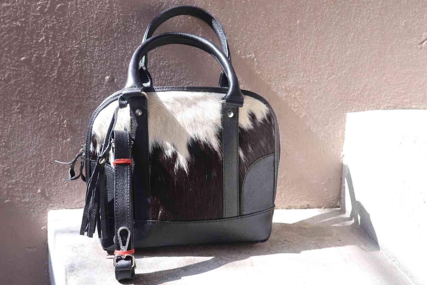 Black and white cowhide handbag on a textured surface. cowhide tote bag for women