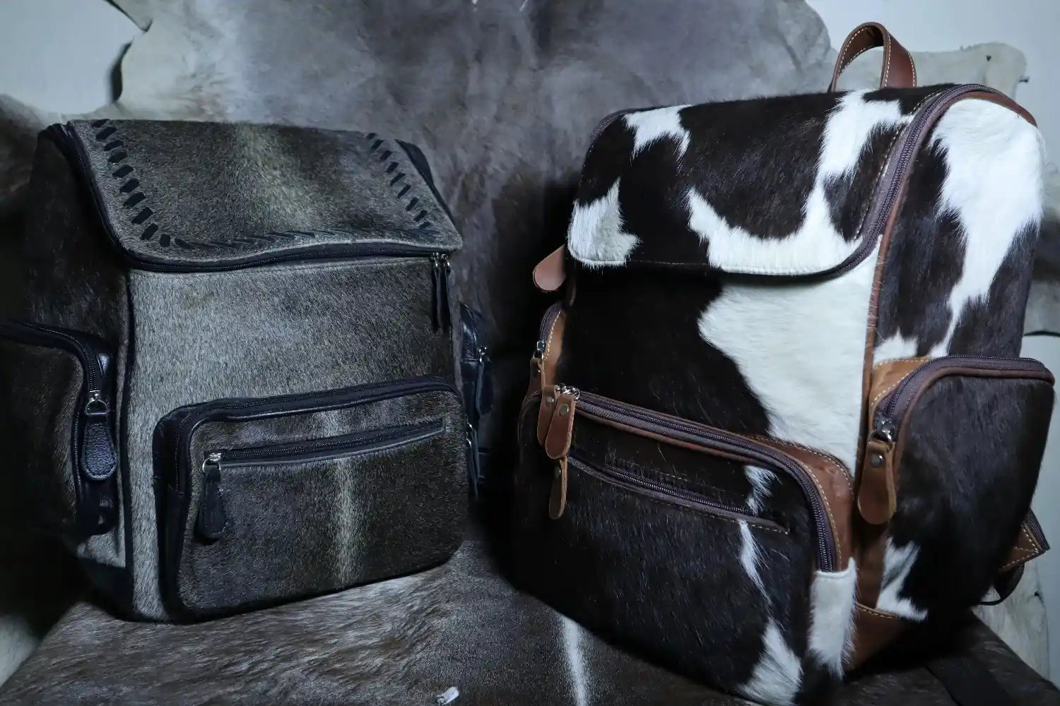Two bags, one gray and one with a cow print, on a textured surface.