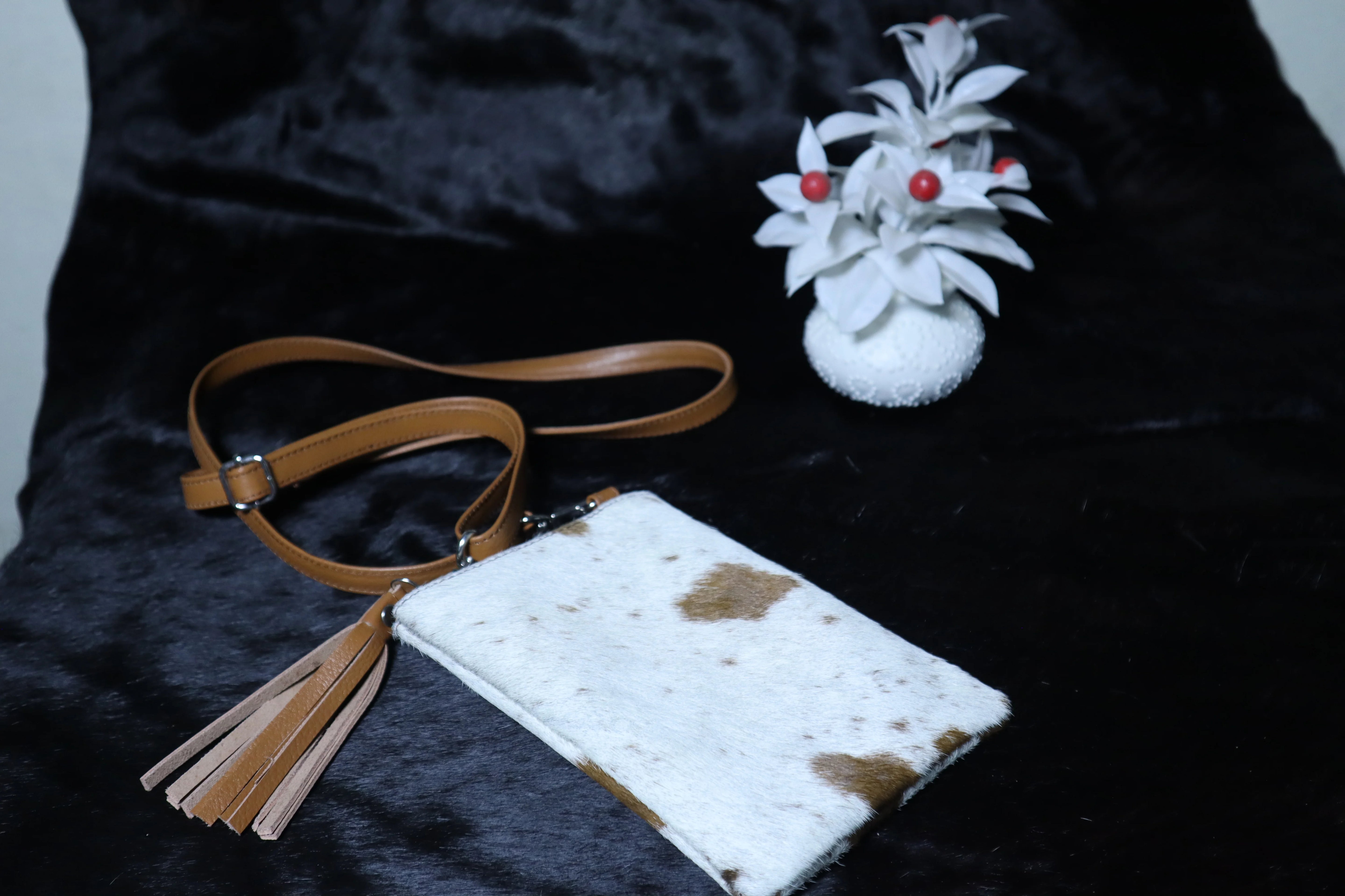 White pouch with brown spots and a brown strap on a dark surface