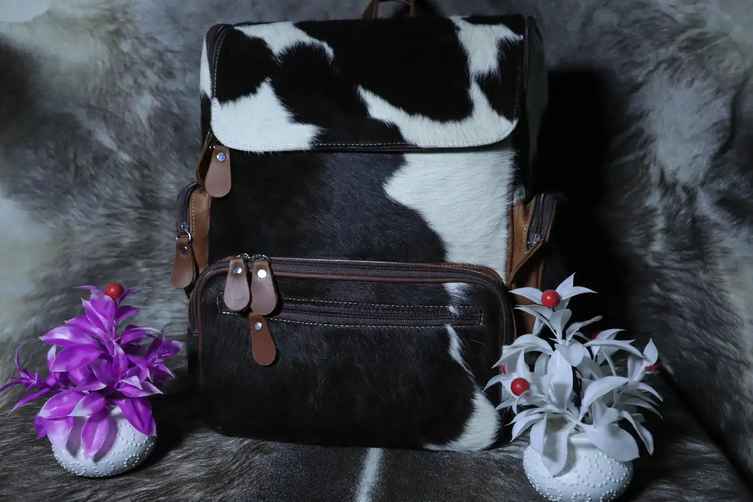 Black and white cow print bag with small decorative plants on a fur-like surface