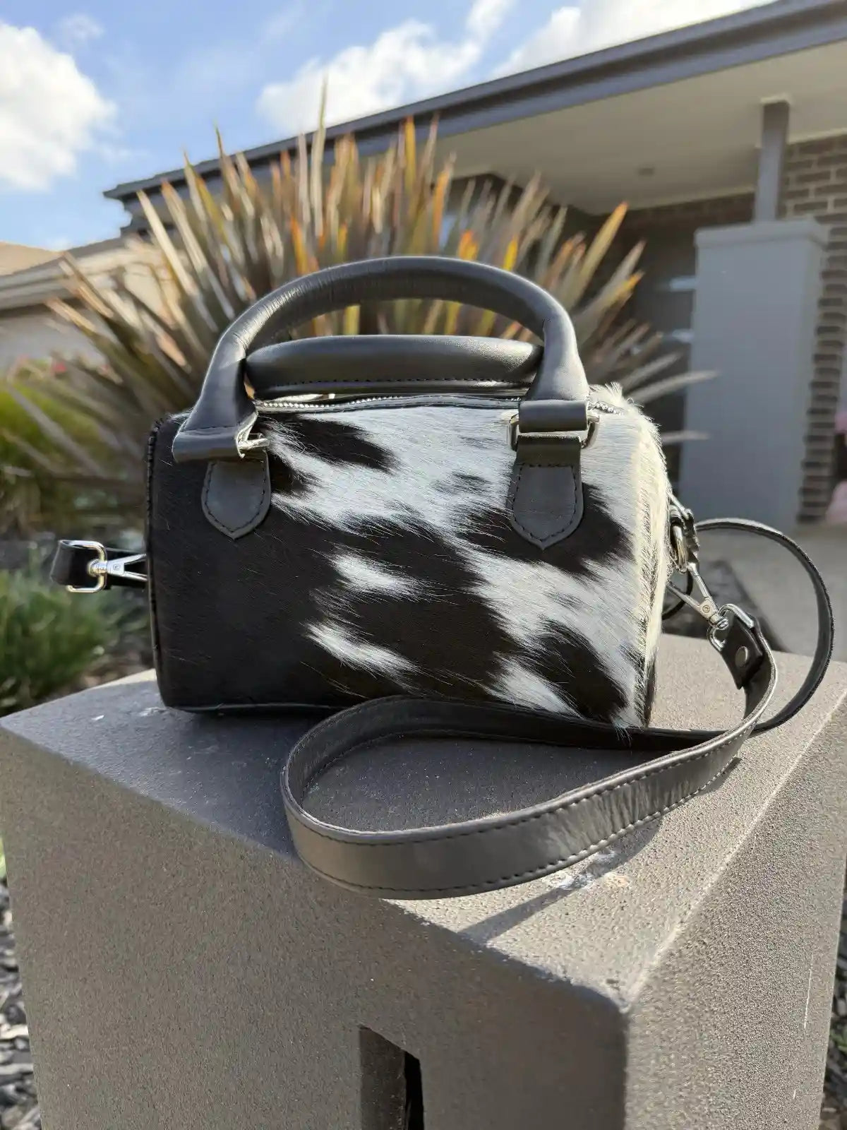 Black and white cow print handbag on a stone ledge with a blurred outdoor background