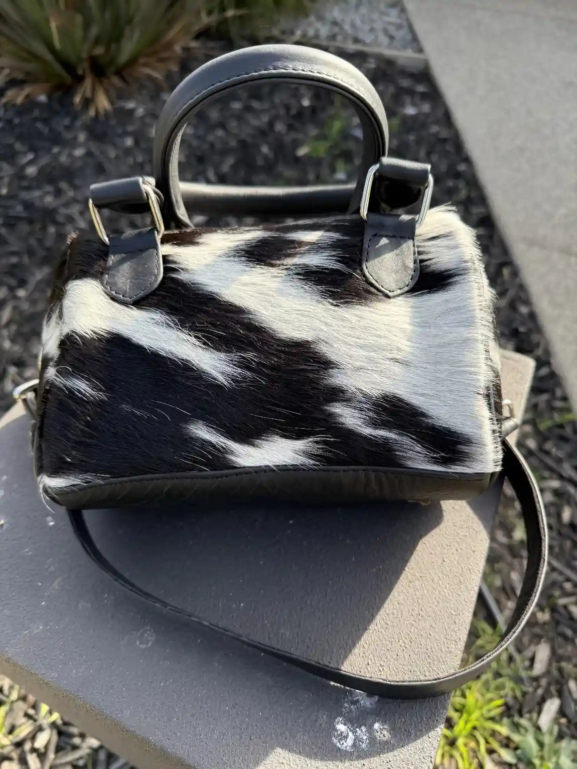 Black and white cowhide handbag on a stone surface with natural background
