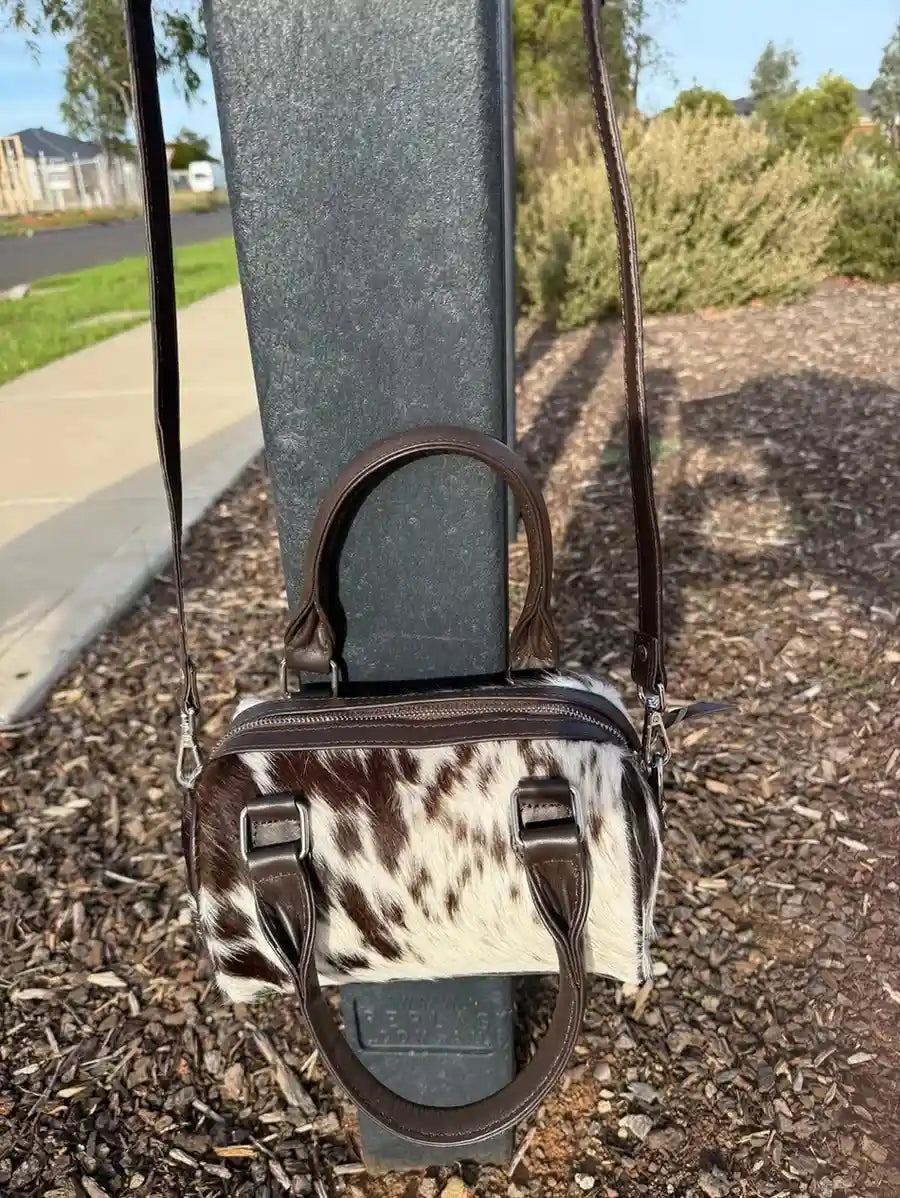 Small handbag with cow print pattern attached to a metal pole outdoors.