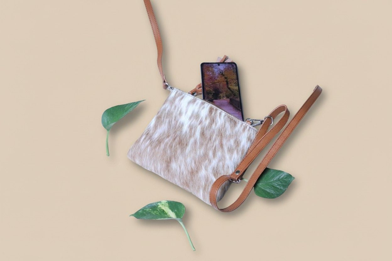 White textured crossbody bag with brown strap and phone on beige background