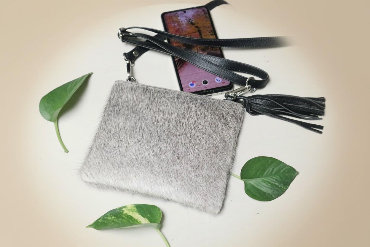 Gray pouch with tassel and phone on a beige background with green leaves