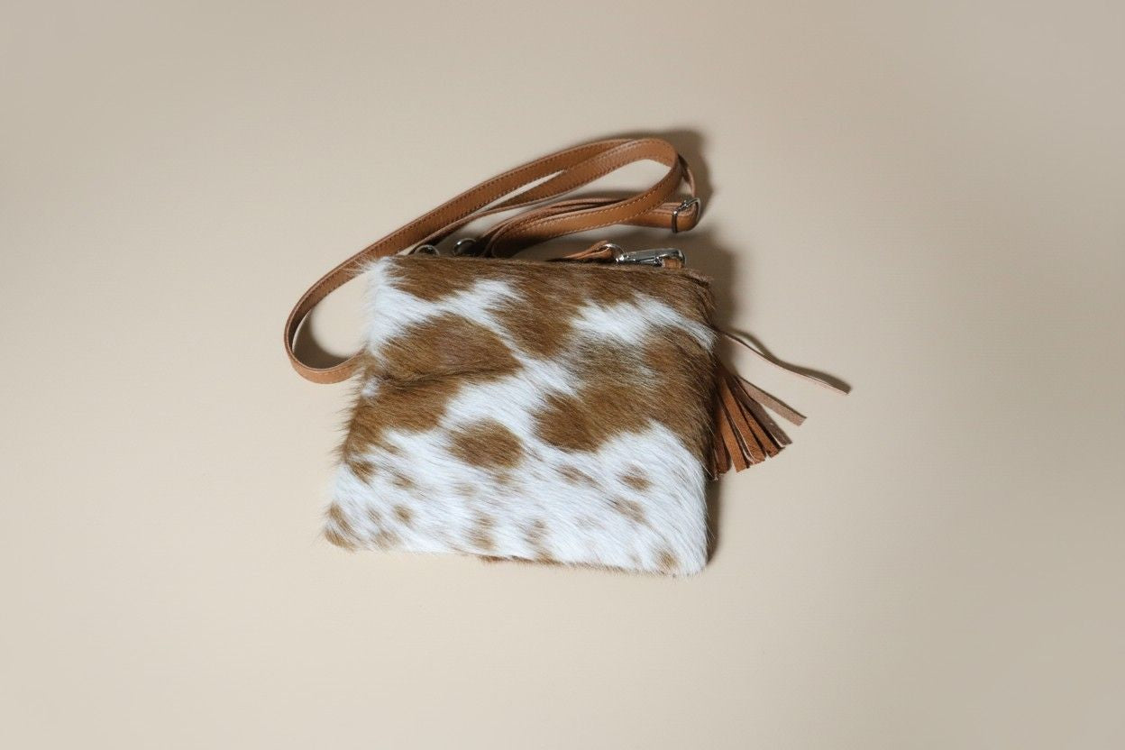Brown and white cowhide leather bag with a strap on a beige background