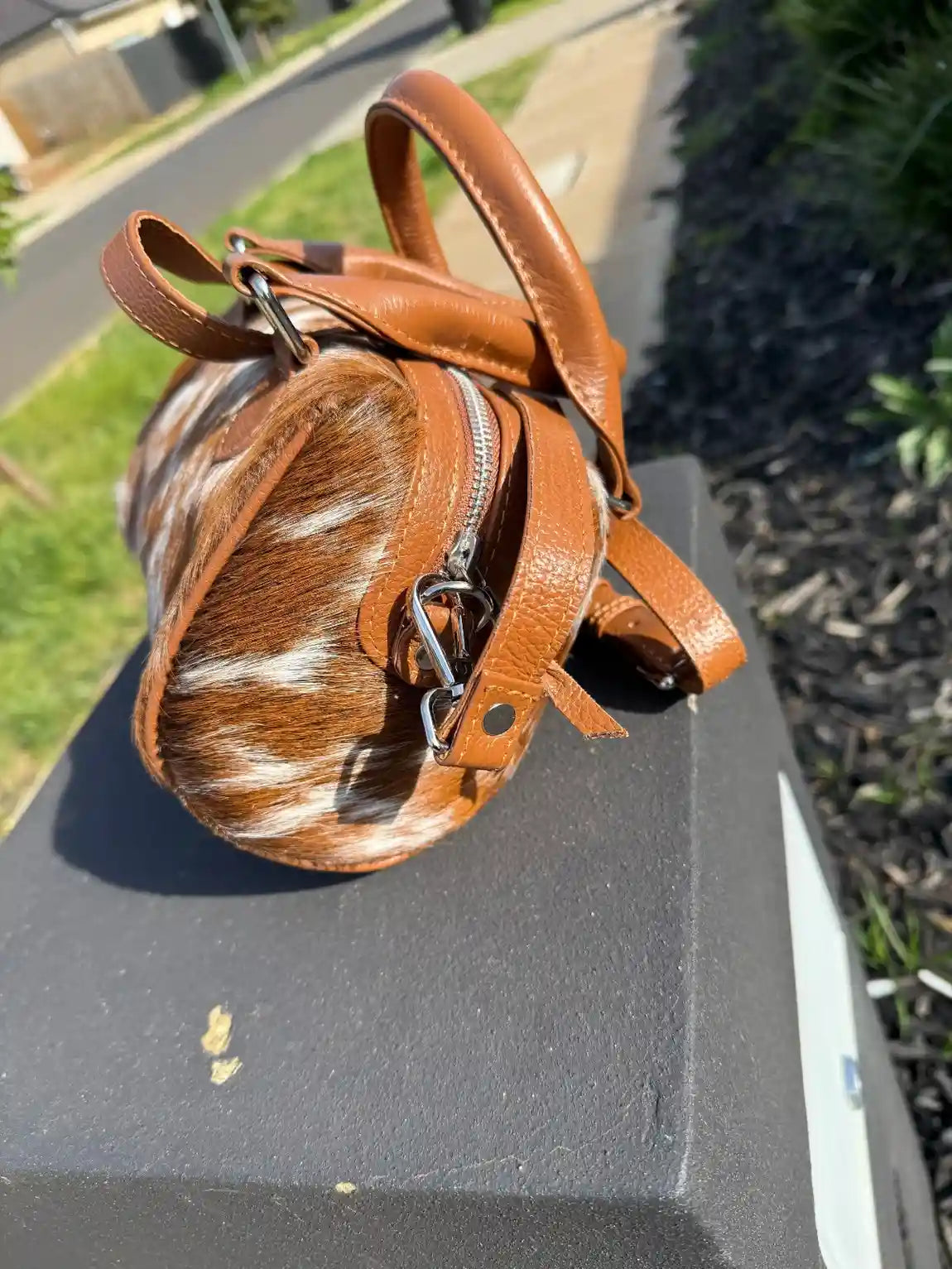 Small brown leather bag with cowhide pattern on a black surface outdoors