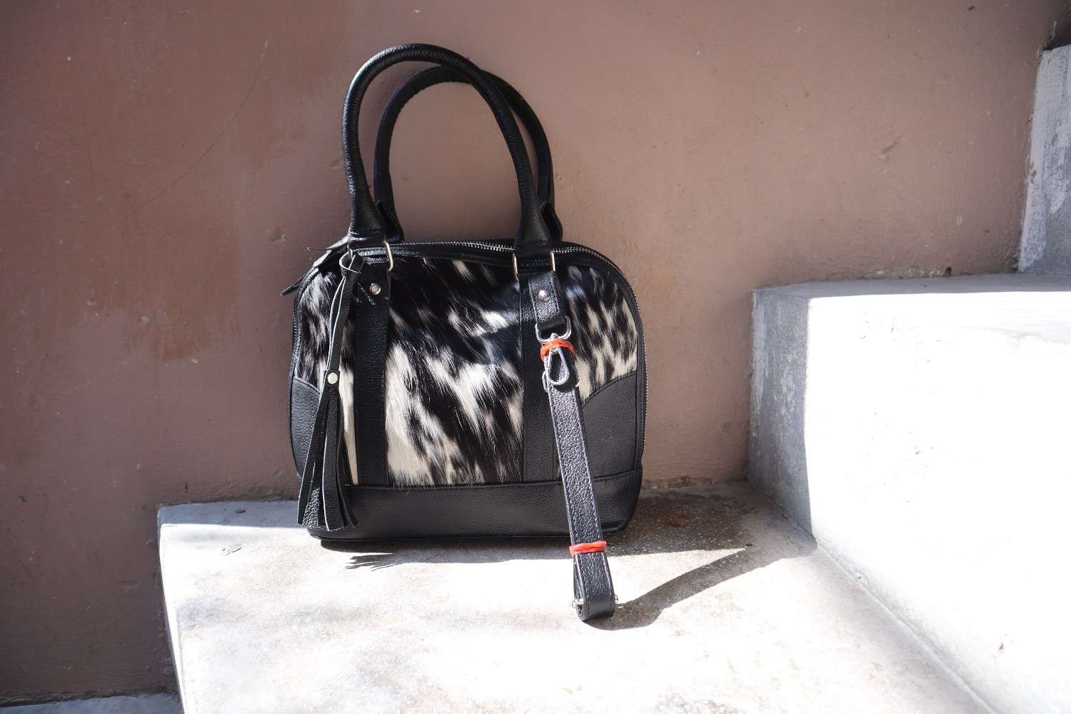 Black and white patterned handbag with a strap on a concrete surface.