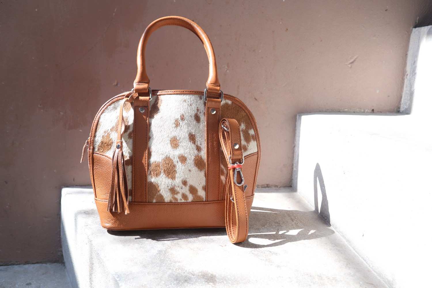 Brown leather handbag with cowhide pattern on a white surface against a beige wall.