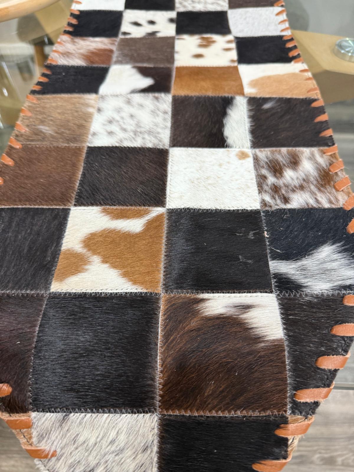 Patchwork cowhide rug with brown, black, and white squares on a wooden floor.