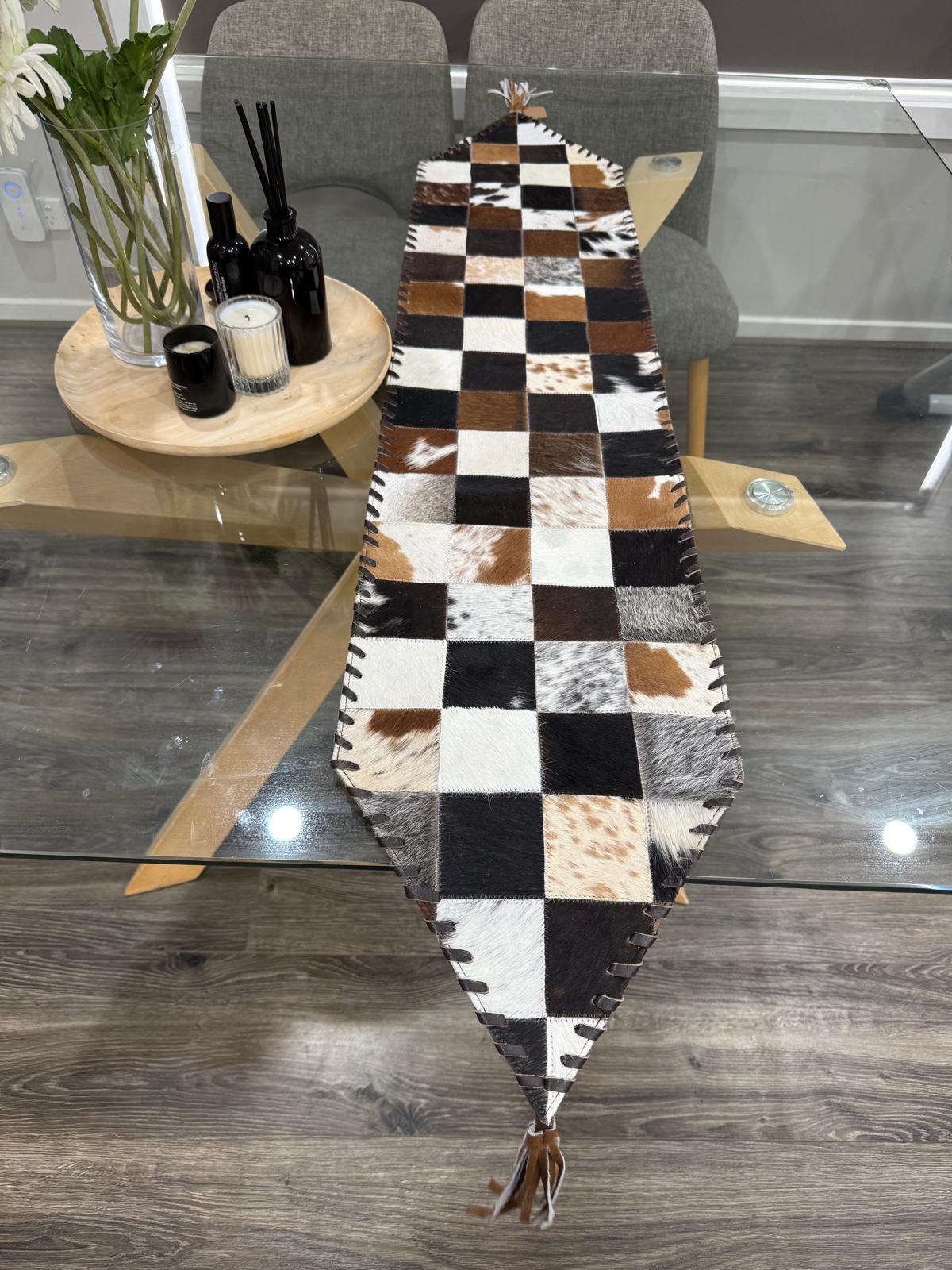 Checkered cowhide rug on a wooden floor with a glass table and chairs in the background.