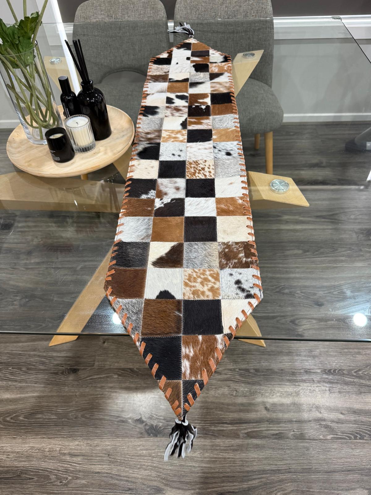 Patchwork cowhide table runner on a wooden table with a modern interior setting.