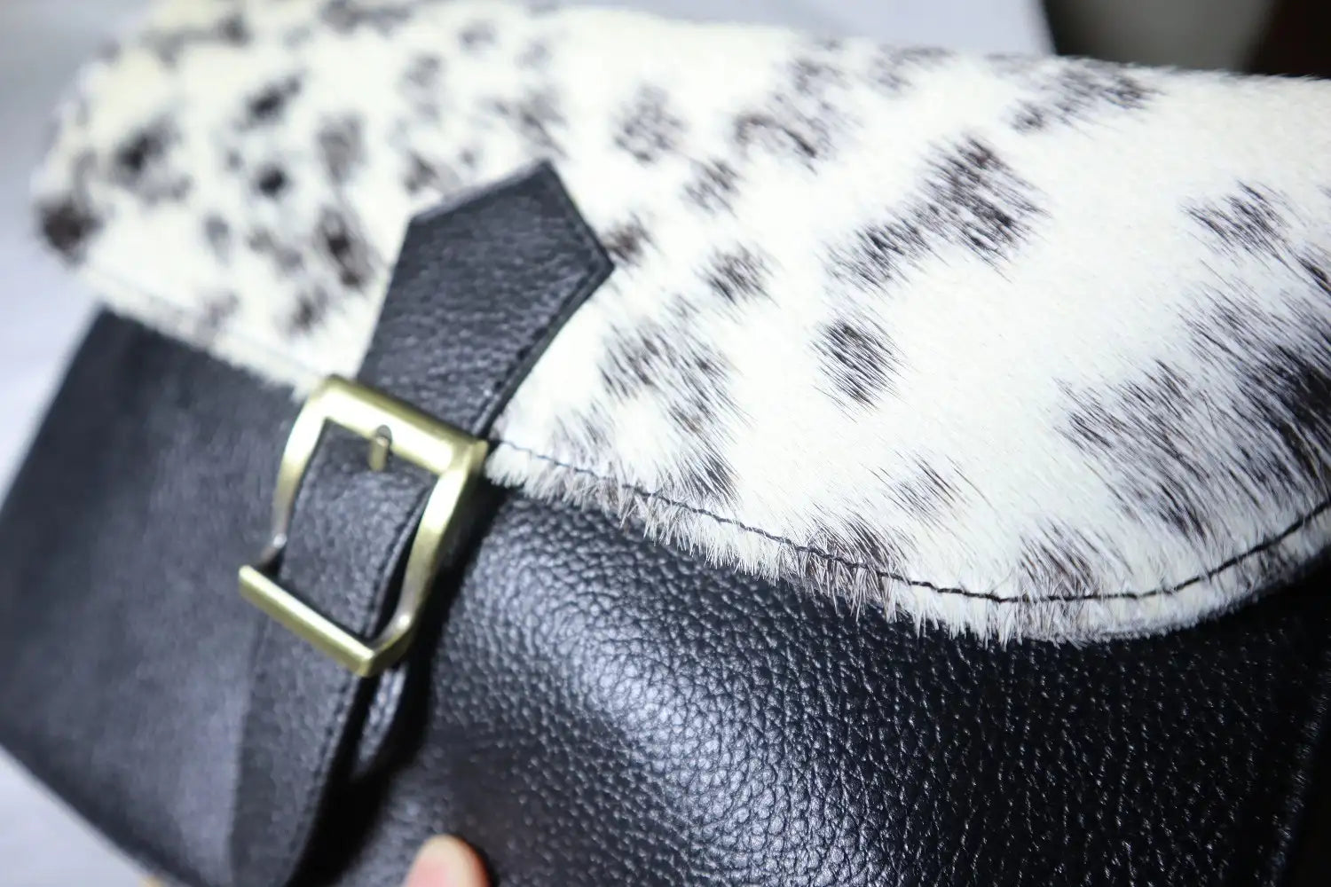 Close-up of a black leather bag with a gold buckle on a white and black patterned fabric background.