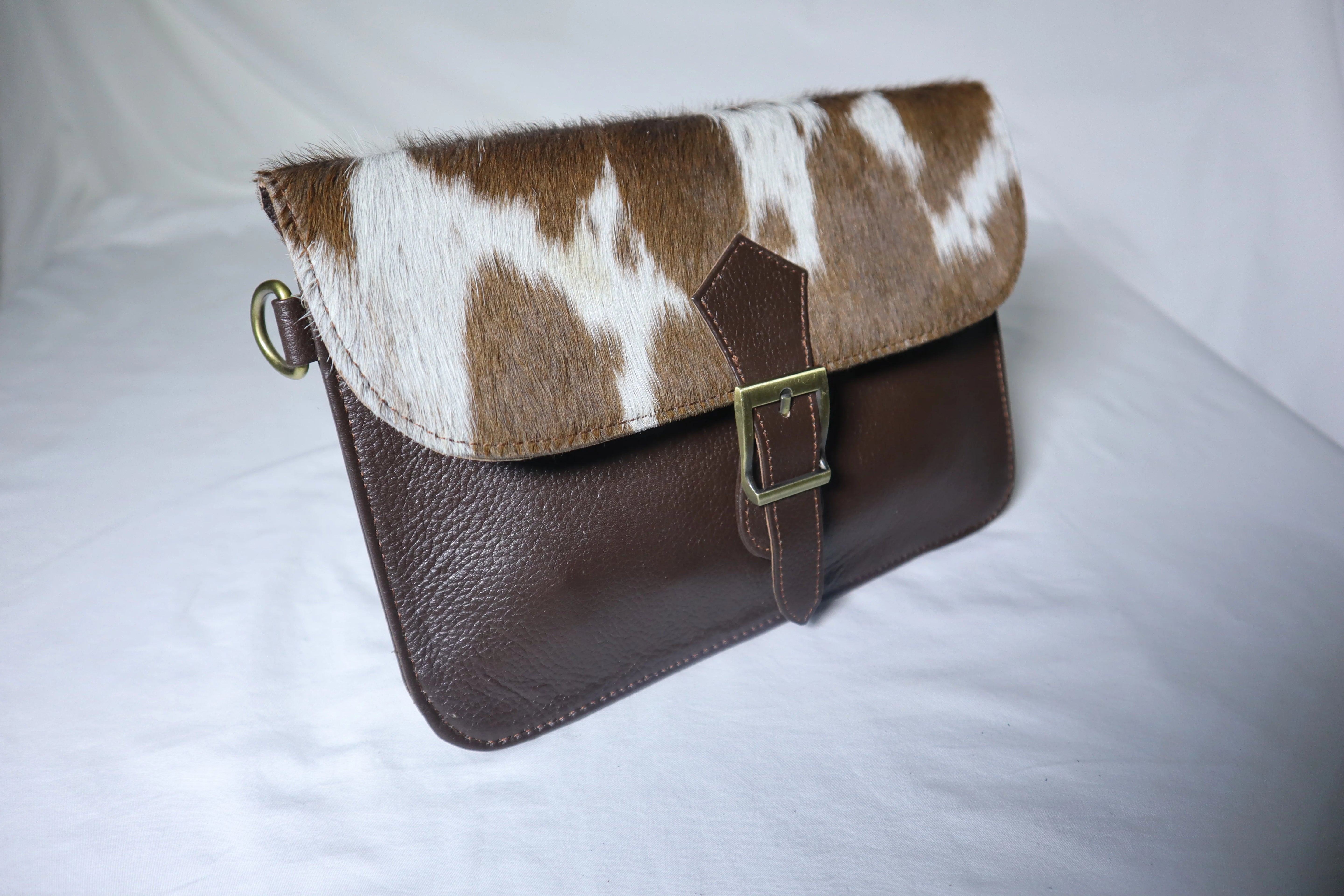 Brown and white cowhide clutch bag on a light gray background