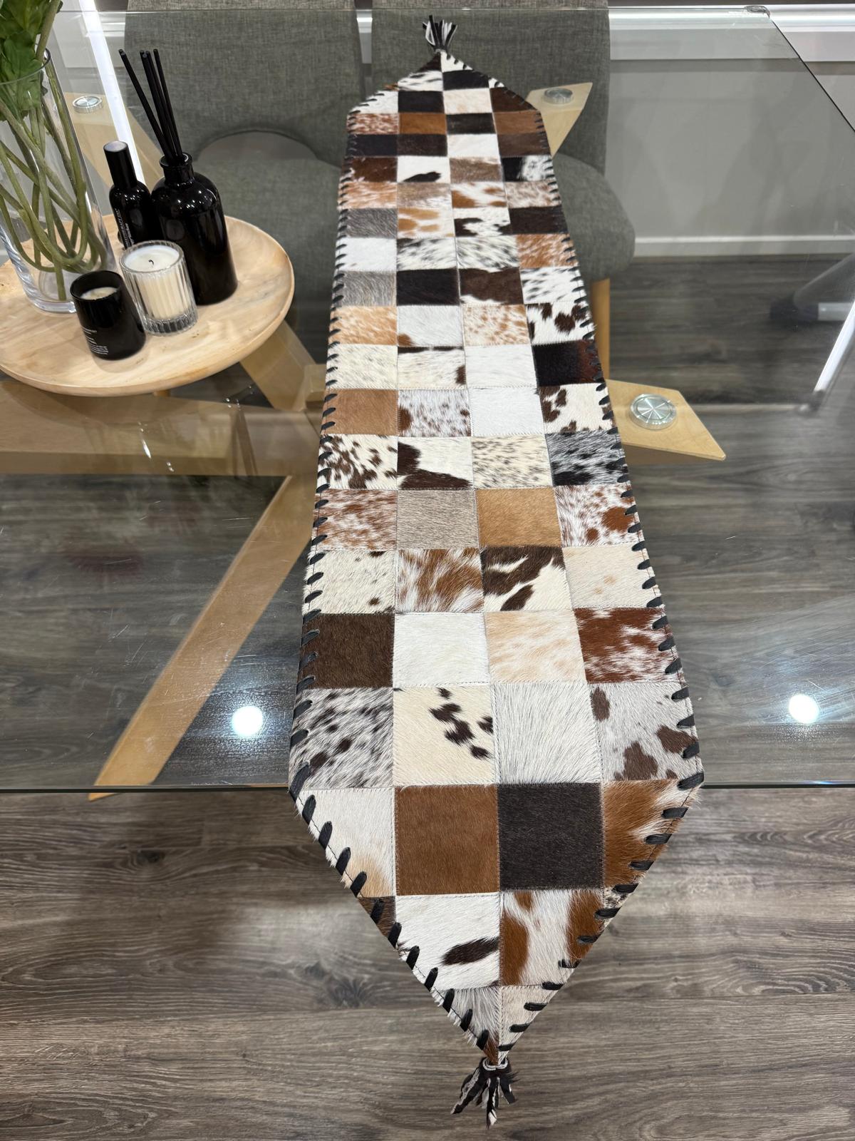 Patchwork cowhide rug on a wooden floor with a glass table and decorative items in the background.