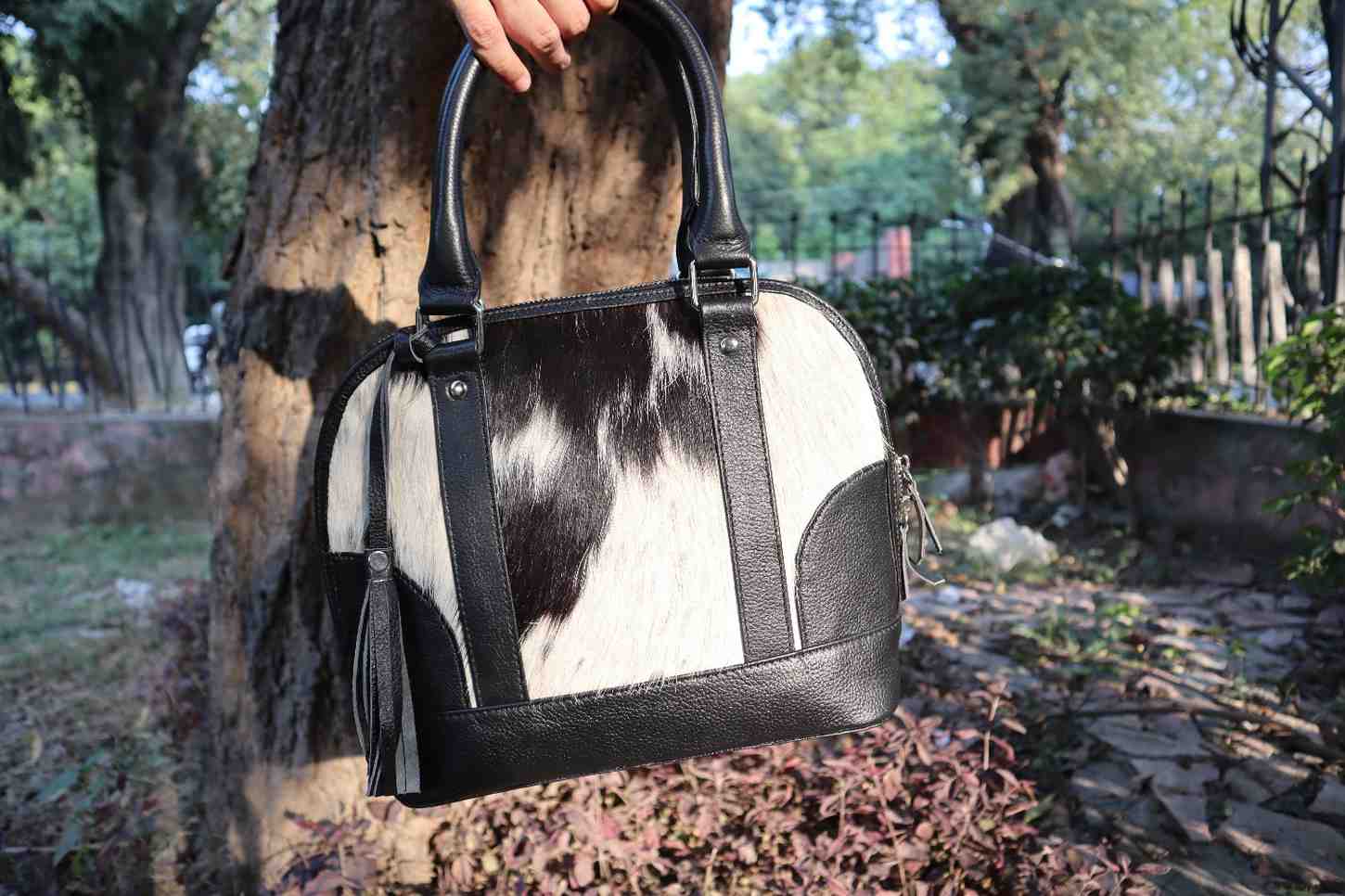 Person holding a black and white cowhide handbag outdoors.
