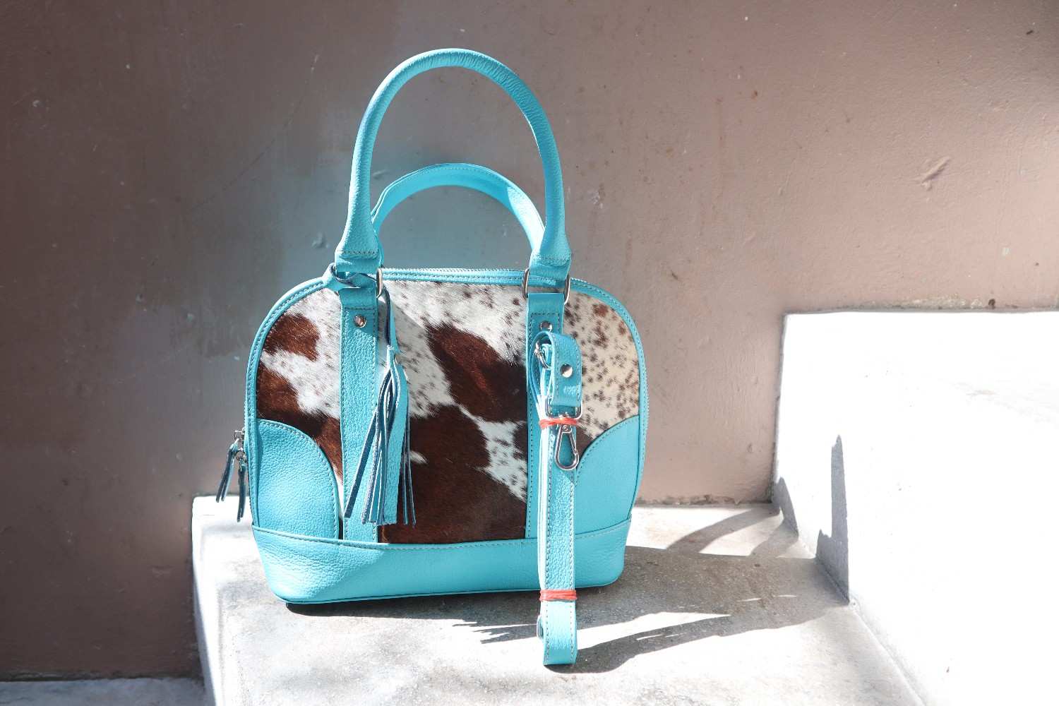 Turquoise handbag with cowhide pattern on a white surface against a beige wall